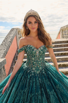 A young woman in a teal sparkly ball gown and tiara stands on stone steps with a cloudy sky behind her.