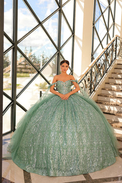 A woman wears a sage green, off-shoulder ball gown with intricate lace detailing near a grand staircase.