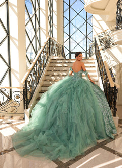 A woman in a seafoam green tulle ball gown poses on an elegant staircase with ornate windows.