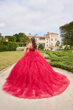 A woman in a vibrant red ballgown stands in a manicured garden with an elegant villa in the background.