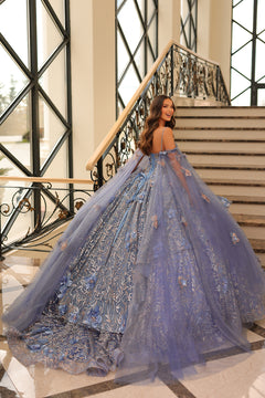 A woman in a lavender ball gown with floral embellishments stands on marble stairs near an ornate railing.