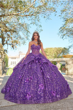 A woman wears a purple floral-embellished ball gown with a tiara, standing outdoors among trees.