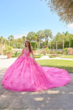 A woman in a vibrant pink butterfly-adorned ball gown stands in a lush garden with palm trees.