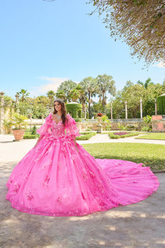 A woman wears a voluminous Fuchsia/Pink floral quinceañera gown in a lush garden setting.