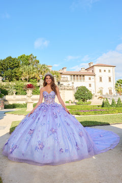 A young woman in a lavender butterfly-adorned ball gown poses in a manicured garden with a grand villa behind her.