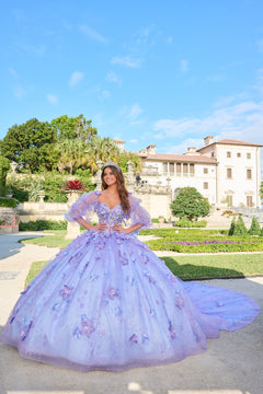 A woman wears a voluminous Lilac/Light Blue ball gown with 3D floral details in a manicured garden.