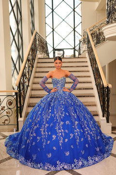 A young woman wears an elaborate Royal Blue ball gown with sparkling embroidery, standing on a grand staircase.