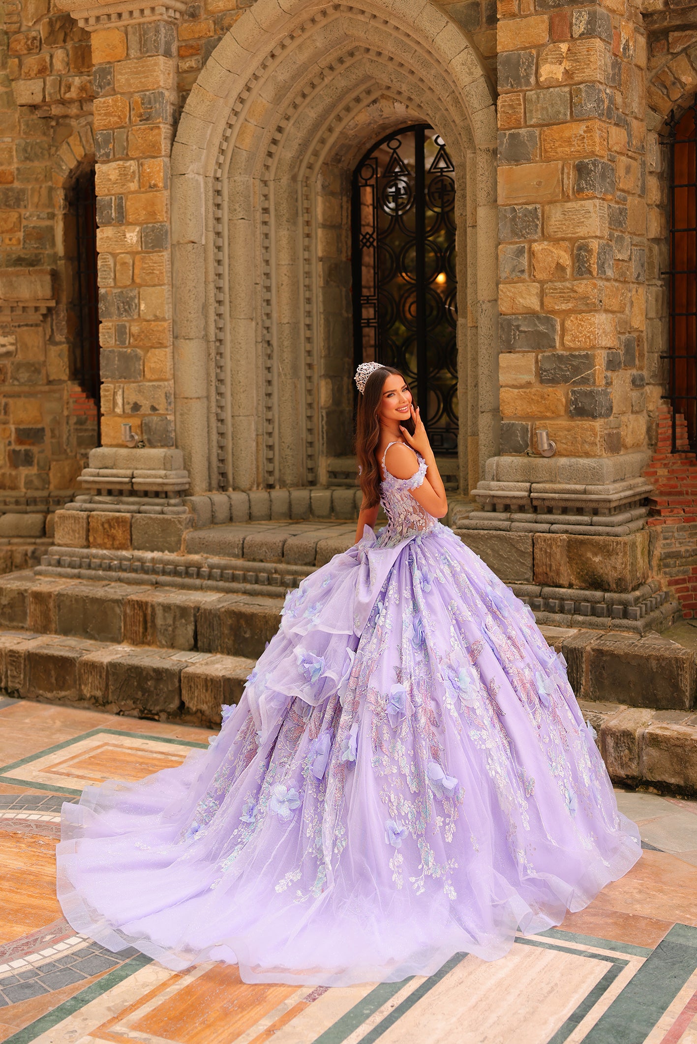 A young woman in a lavender ball gown stands before a stone archway, wearing a delicate tiara.