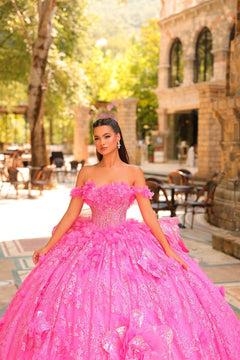 A woman in a voluminous hot pink ball gown stands in a sunlit stone courtyard with tables and trees.