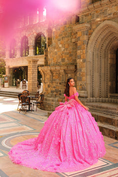 A person in a voluminous, bright pink ball gown poses in front of an ornate stone building with arched windows.