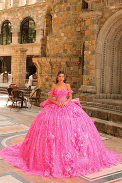 A woman wears a voluminous fuchsia off-shoulder ball gown with 3D floral details in a stone castle setting.