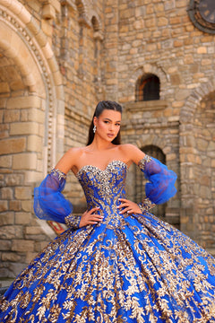 A woman wears a royal blue and gold sequined ball gown with puffy sleeves, posing in a stone castle.
