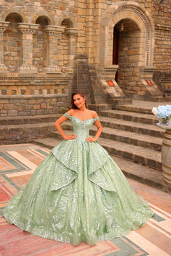 A woman wears a sage green off-shoulder ballgown with sparkling details in front of a stone building.