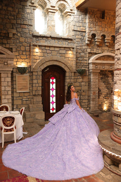 A young woman in a lavender ball gown poses dramatically in a stone castle-like interior with arched windows.