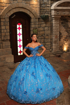 A woman wears a turquoise off-shoulder ball gown with intricate floral embroidery in a stone castle setting.