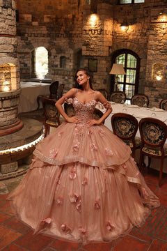 A woman wears a rose gold ballgown with 3D floral details, posing in a stone castle interior.