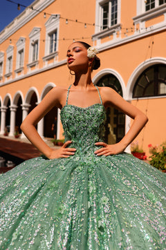 A model wears a sage green sequined ball gown with a corseted bodice, standing confidently against an orange building.