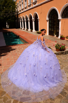 A woman wears a lavender ball gown with 3D floral details, posing by a pool near an arched terracotta building.