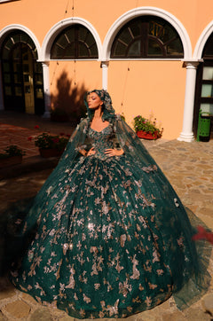A woman in an emerald green ball gown with silver floral embellishments poses dramatically in an arched courtyard.