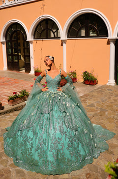 A dramatic sage green quinceañera ball gown with sparkling embellishments, worn on a stone courtyard with arched windows.