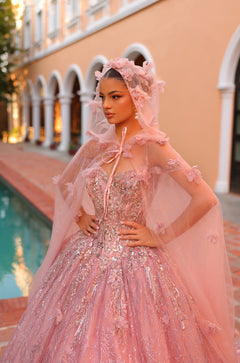 A woman wears a sparkling pink ballgown with intricate lace details and a flowing veil in an arched architectural setting.