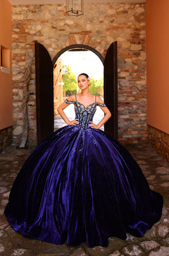 A woman in a royal blue ballgown poses confidently in a stone archway with her hands on her hips.