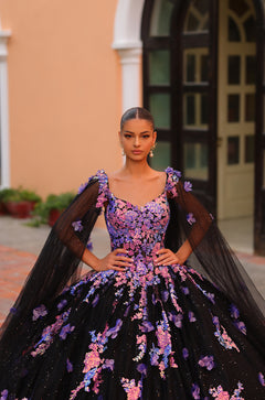A model wears a black ball gown with purple and pink floral embroidery and sheer cape-like sleeves.