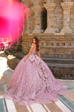 A young woman wears a lavender lace ball gown with an off-shoulder design, posing on stone steps.