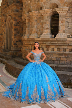 A woman in a voluminous Turquoise/Gold quinceañera dress poses confidently before an ornate stone architectural backdrop.