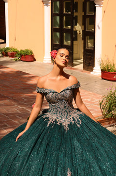 A woman in a shimmering green ball gown stands in a sunlit courtyard with a flower in her hair.