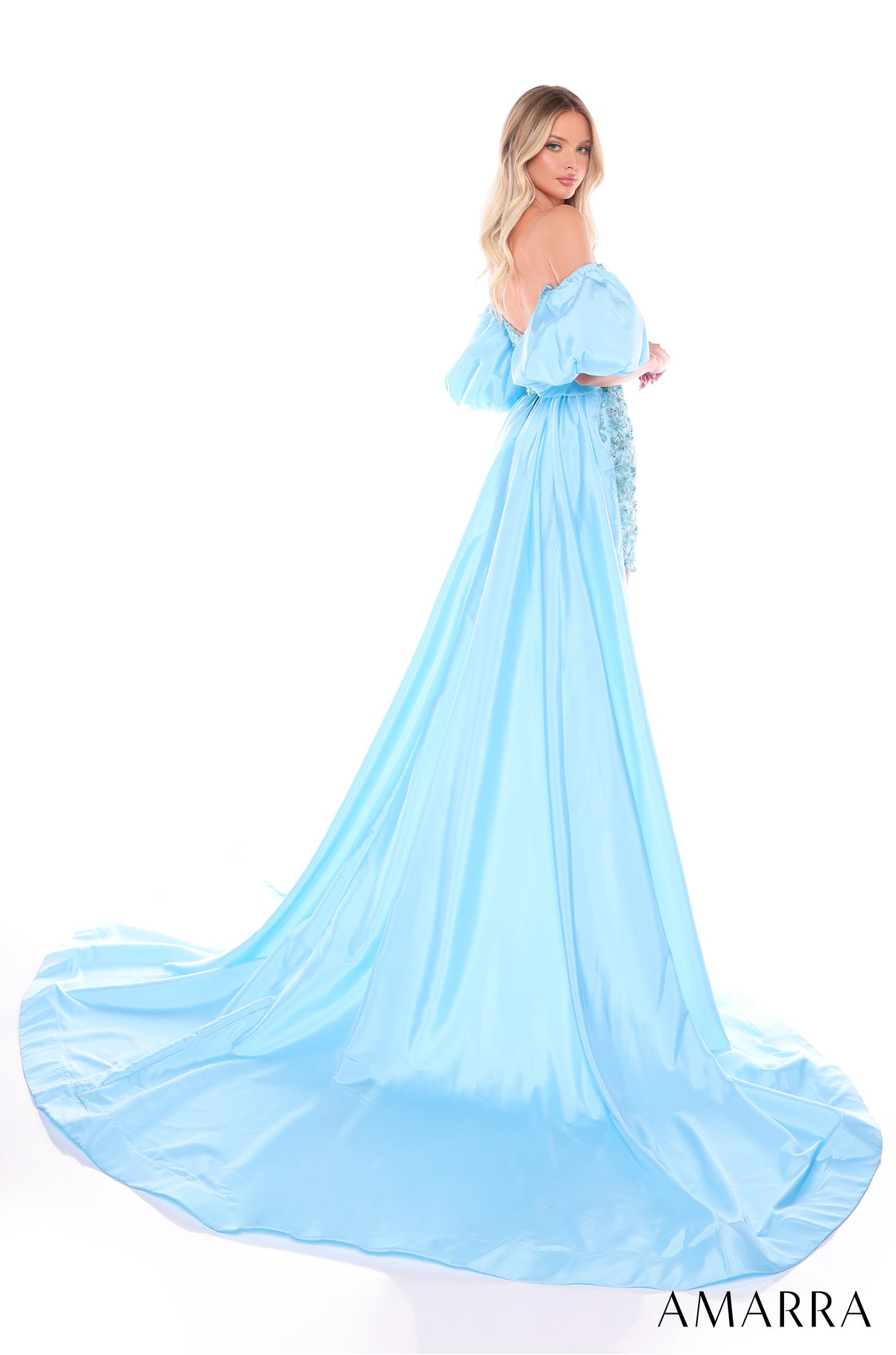 A woman wears an off-shoulder blue ballgown with voluminous sleeves and a sweeping train against a white background.