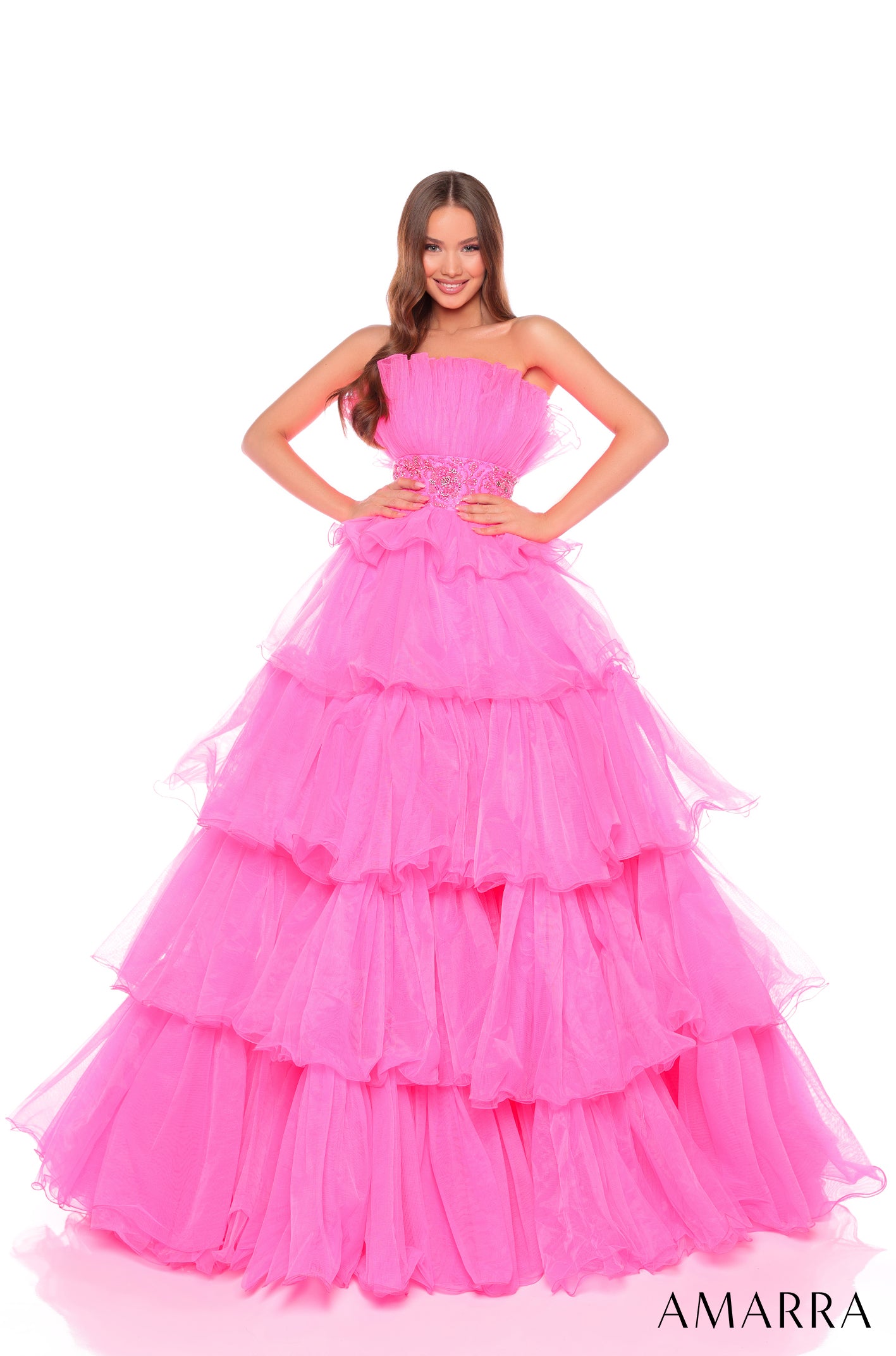 A woman wears a strapless, tiered Hot Pink ball gown with a beaded waistline by Amarra.