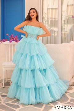 A woman wears a strapless, light blue tiered ball gown with ruffled layers on a stone patio.