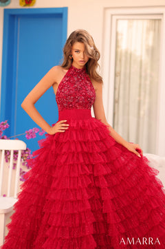 Model wears a red tiered, sequined halter ball gown with a fitted bodice against a blue and white backdrop.