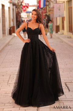 A woman stands confidently in a voluminous black lace ball gown on a cobblestone street.