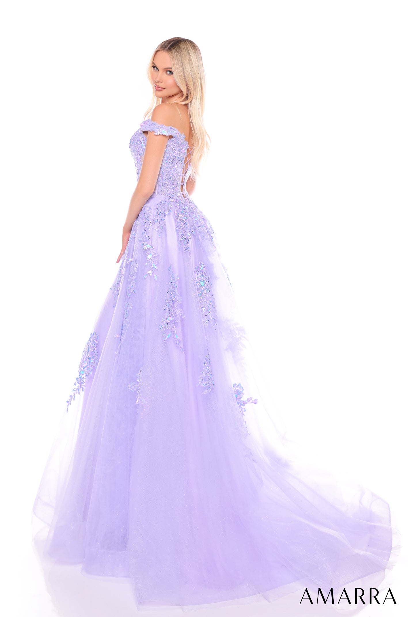 A blonde model wears a lavender off-shoulder ball gown with floral embellishments and a flowing tulle skirt.