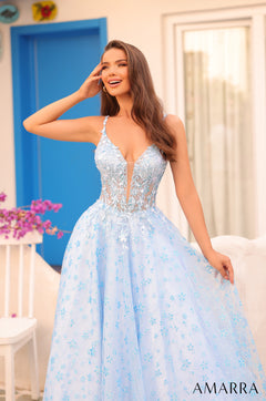 A woman in a light blue floral ballgown with a plunging neckline, smiling and posing elegantly.
