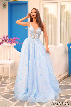 A woman wears a light blue floral ball gown with a corseted bodice, standing against a blue door.