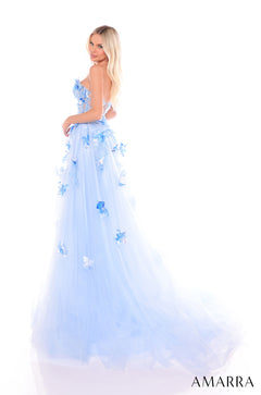 A blue tulle ball gown with 3D floral appliqués, worn by a blonde model against a white background.