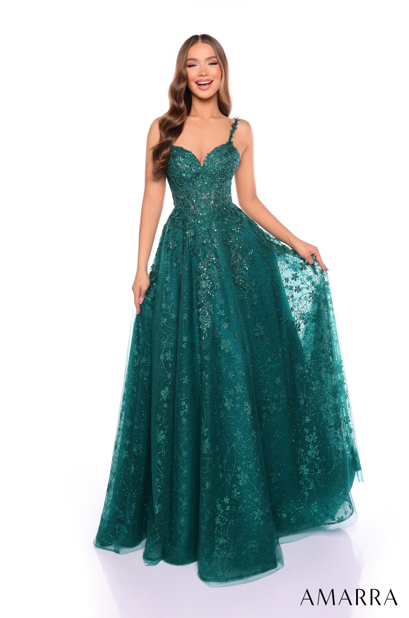 A woman wears a floor-length emerald green ball gown with sparkling lace and a sweetheart neckline.