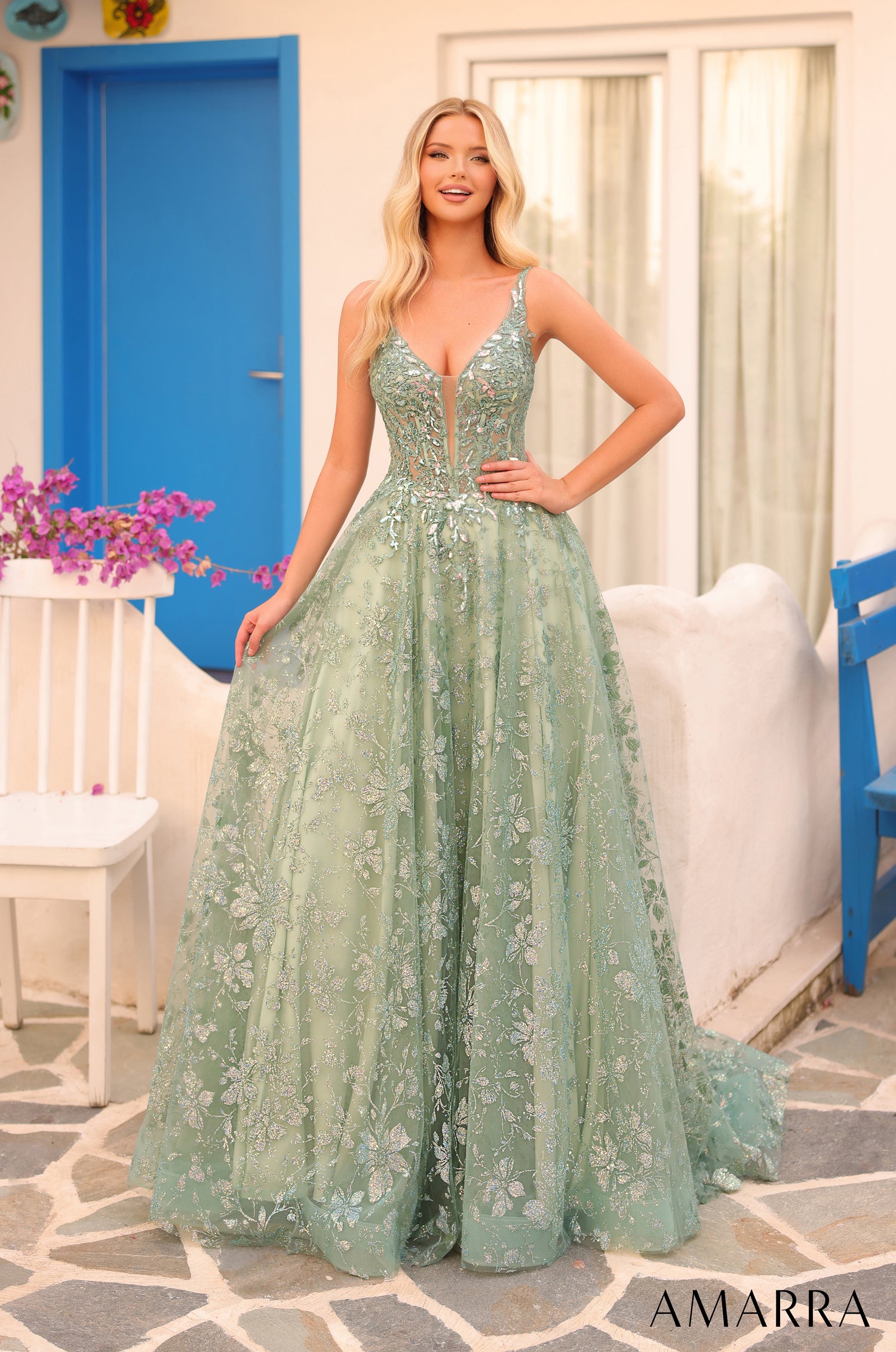 A blonde woman wears a flowing avocado green lace ball gown with floral embroidery against a blue door backdrop.