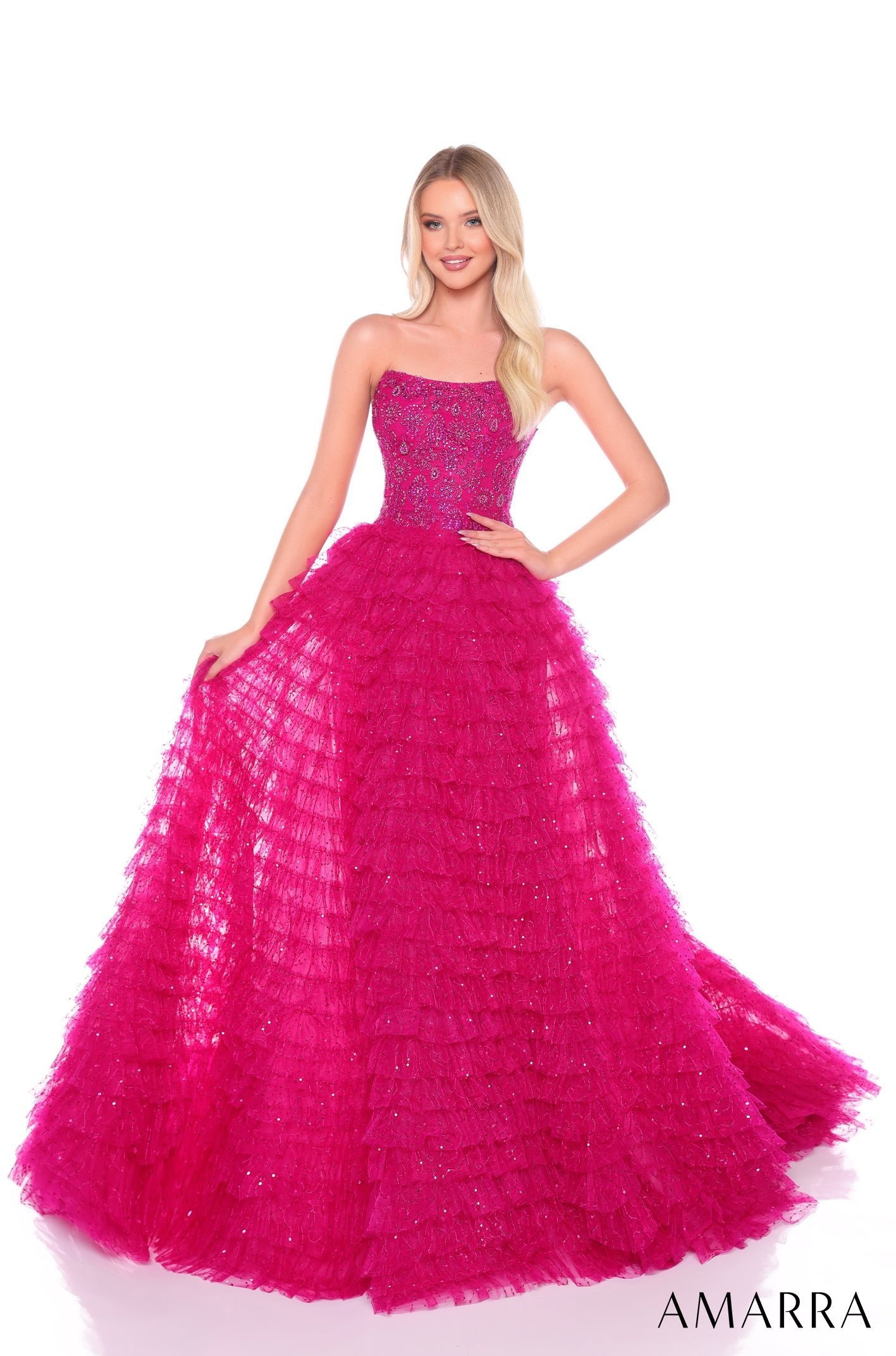 A woman models a strapless, tiered Bright Fuchsia ball gown with sparkling embellishments from Amarra.