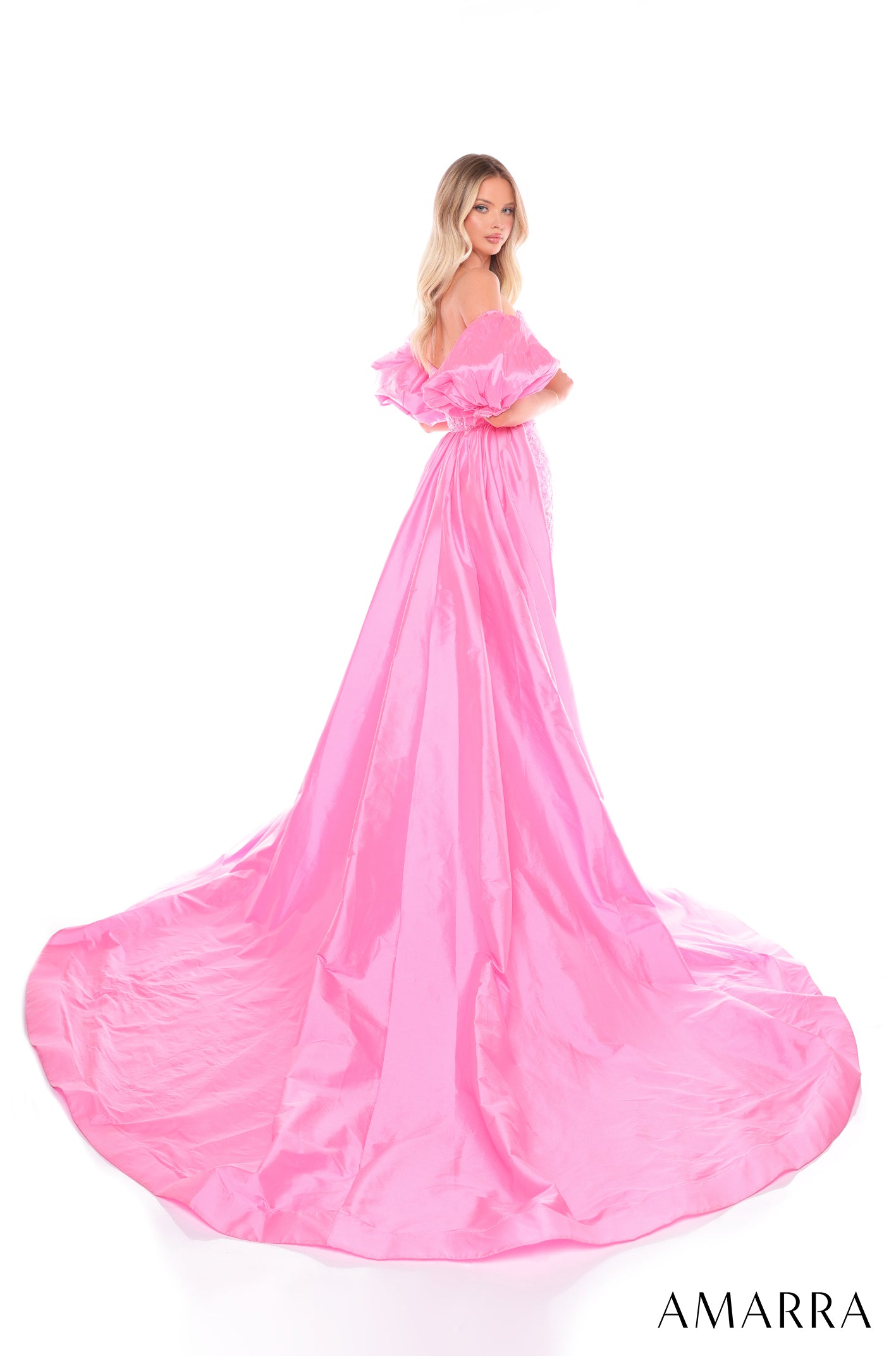 A blonde woman wears a voluminous, bright pink off-shoulder ball gown with a long, flowing train.