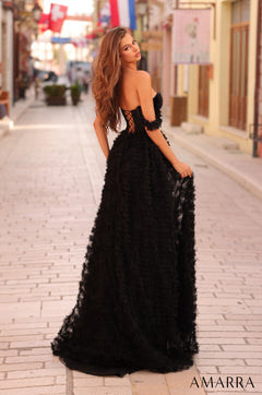 A woman in a black, floor-length gown with textured fabric stands on a brick street, looking over her shoulder.