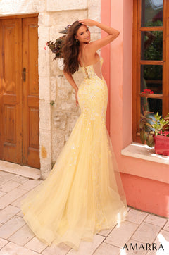 A model wears a flowing yellow sequined mermaid gown with a corset bodice, standing by a stone wall.