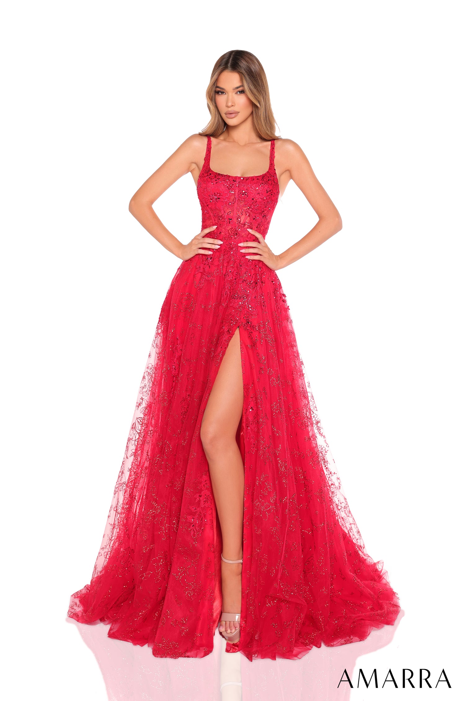 A model wears a floor-length red lace gown with a high slit and sparkling embellishments by Amarra.