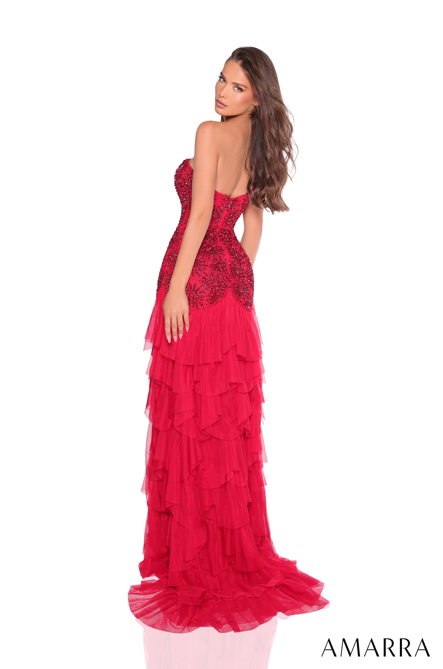A woman wears a red sequined strapless gown with tiered ruffled skirt, posing in a full-length profile view.