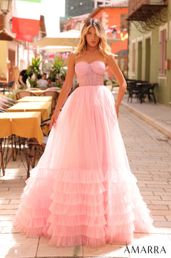 A woman wears a strapless, voluminous light pink tulle ball gown standing on a cobblestone street with cafe tables.