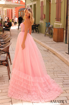 A woman wears a voluminous pink tulle gown with a strapless bodice, standing on a charming cobblestone street.