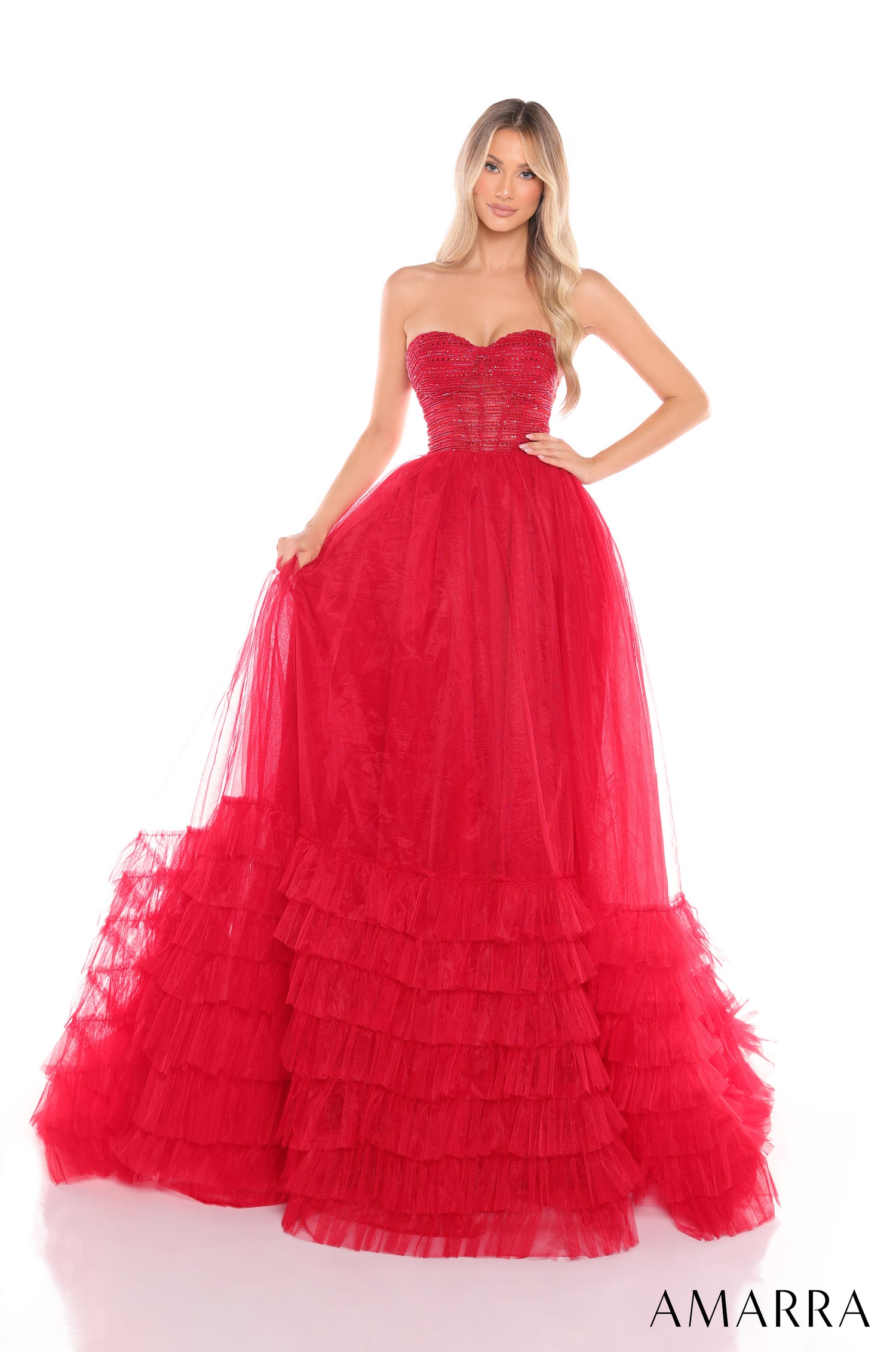 A model wears a strapless, tiered red tulle ball gown with a fitted bodice and full, ruffled skirt.